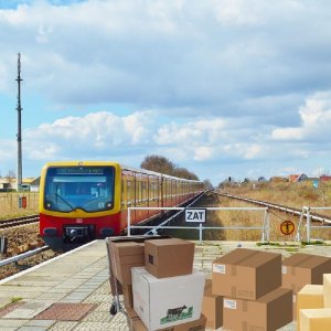 Eine S-Bahn fährt in ein Bahnhof ein. Auf dem Bahnsteig stehen Kartons.