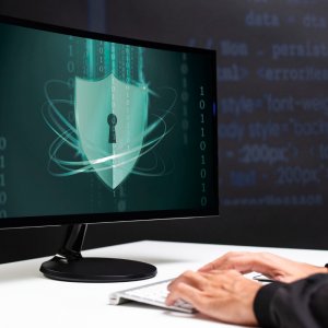 Hände auf Tastatur vor Bildschirm mit Schloss geschlossen und umgeben von Matrix