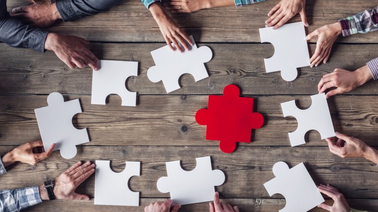 Partner im Cluster werden Tisch von oben mit übergroßen Puzzleteilen und Händen die danach greifen